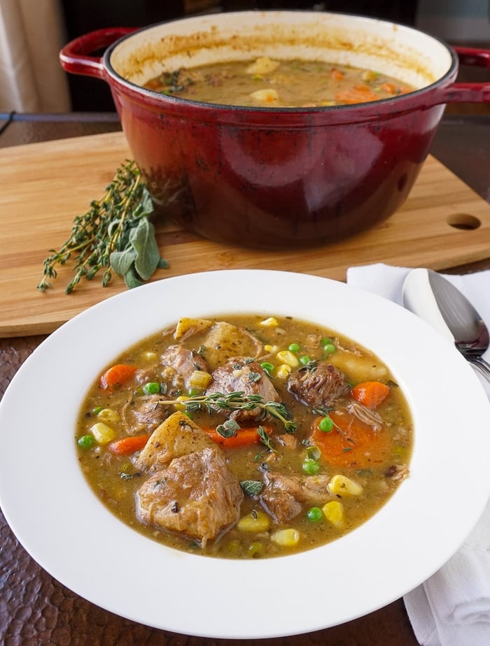 Pork Stew in a white bowl with pot of stew in the background