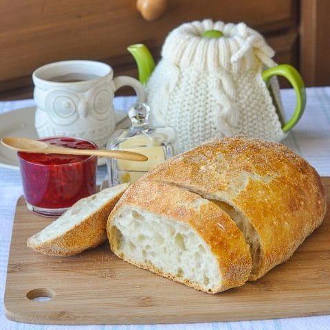 No knead Bread on a wooden cutting board with butter, jam and tea in the background