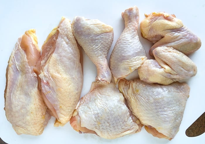 One whole chicken on a white plastic cutting board cut into 8 pieces