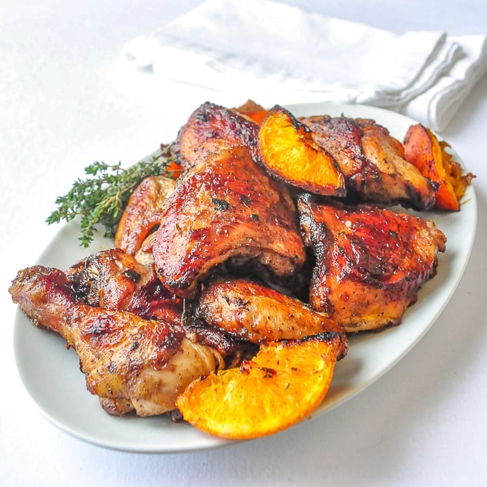 Orange Broiled Chicken on a white platter with orange wdge garnish