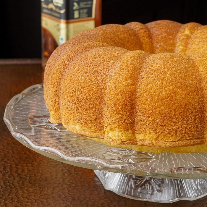 Jamaican Rum Cake on a clear glass pedestaal with bottle of rum in background