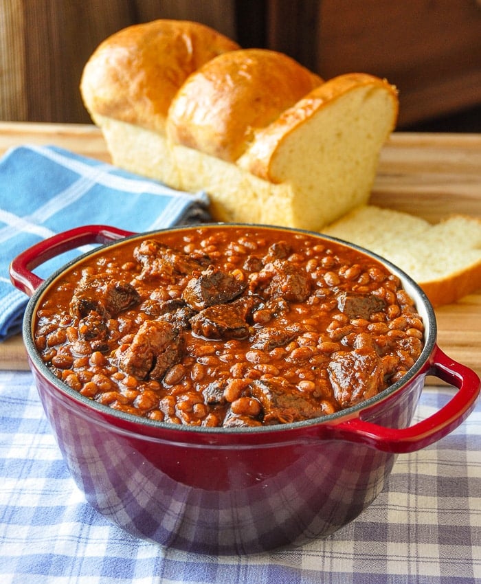 Maple Chipotle Pulled Pork and Beans in a red dutch oven with fresh baked bread in background