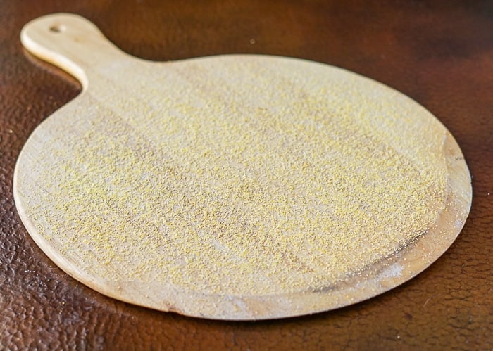 Cornmeal scattered evenly onto a round wooden peel