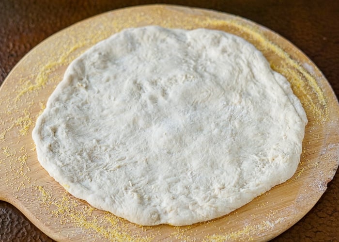 Pizza dough cretched and resting on a wooden peel.