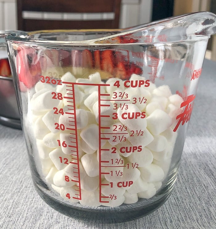 Marshmallows in a clear glass measuring cup.