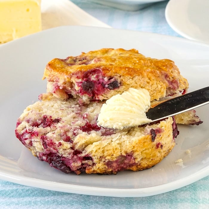 Close up photo of a single scone being spread with butter