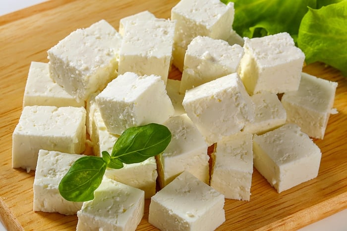 Stock photo of feta cheese with basil leaves on a wooden cutting board