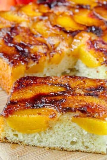 Peach Upside Down Cake close up photo of a single sice on a wooden cutting board.
