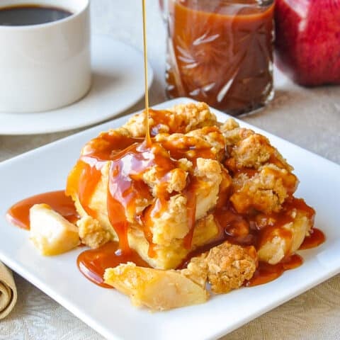 Apple Crumble Bread Pudding on a white plate with caramel, apple and coffee in the background