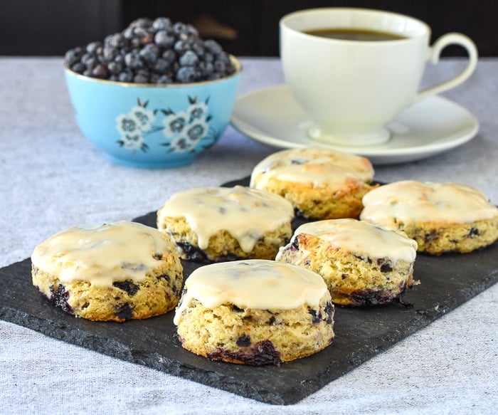 Blueberry Tea Buns on a slate serving plate with a bowl of blueberries and a cup of tea in the background