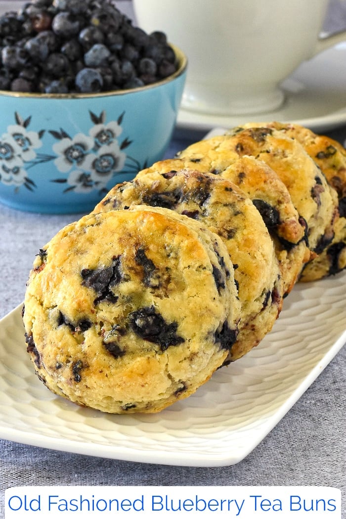 Blueberry Tea Buns on a white plate with blueberries in background with title text added for Pinterest