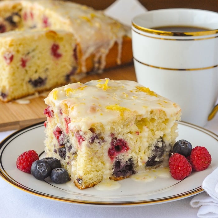 photo of a single slice of Lemon Drizzle Cake with Blueberries and Raspberries shown on a white and gold tea service