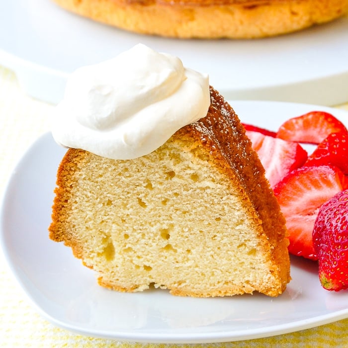Close up photo of a singe slice of the Best Vanilla Pound Cake recipe shown with strawberries and whipped cream
