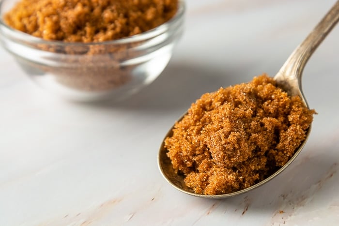 Brown sugar in metal spoon on bright, marble background