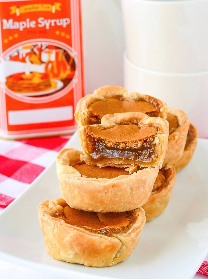 Maple tarts stacked on a rectangular white platter with a can of maple syrup in the background