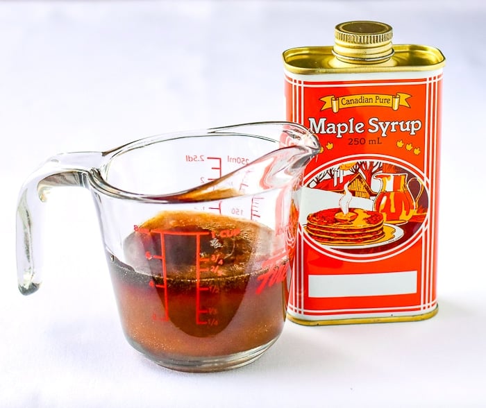 Simmered maple syrup in a glass measuring cup beside a can of maple syrup