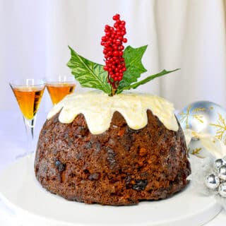 Christmas Plum Pudding with glasses of brandy and Christmas decorations on a white serving platter