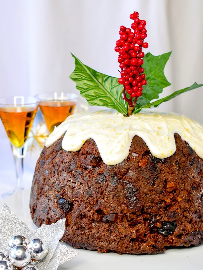 Completed Christmas Plum Pudding surrounded by Christmas decorations with a sprig of holly inserted in the top