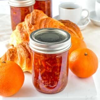 One jar of clementine marmalade pictured with croissants and fresh clemntines