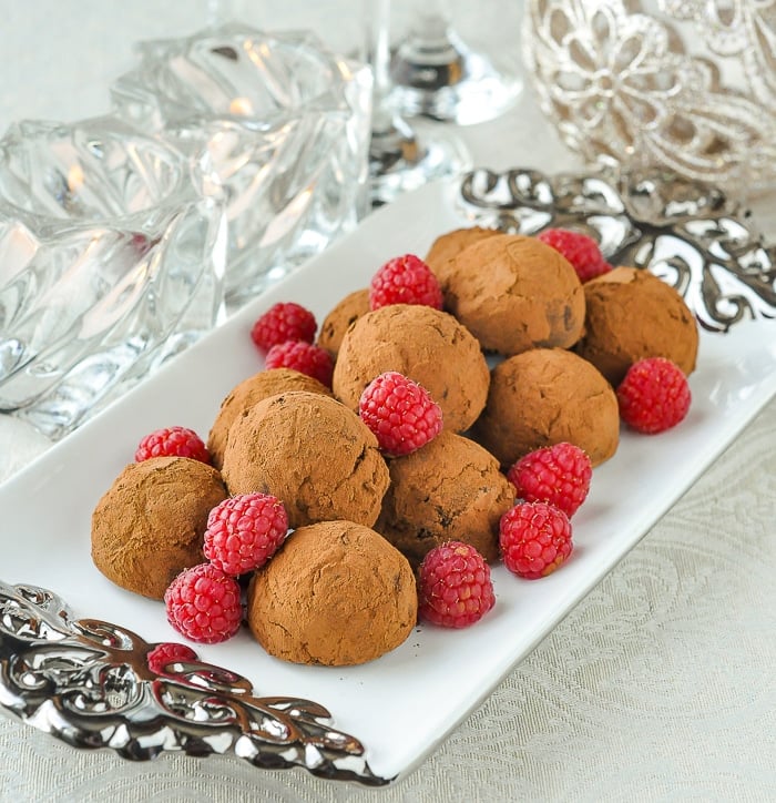 Raspberry Chocolate Truffles on a white and silver platter with candles and Christmas decorations in the background