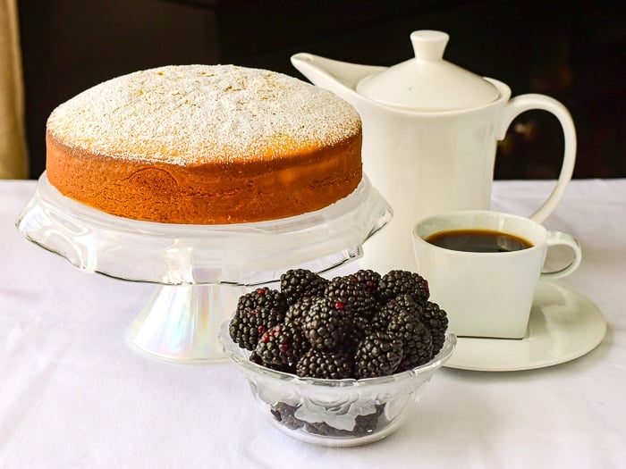 Condensed Milk Cake shown uncut with a white coffee service and blackberries