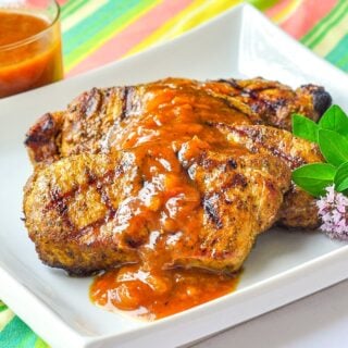 Curry Pork Chops with Easy Plum Chutney on a white plate with oregano garnish