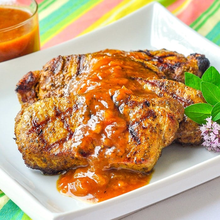 Curry Pork Chops with Easy Plum Chutney on a white plate with oregano garnish