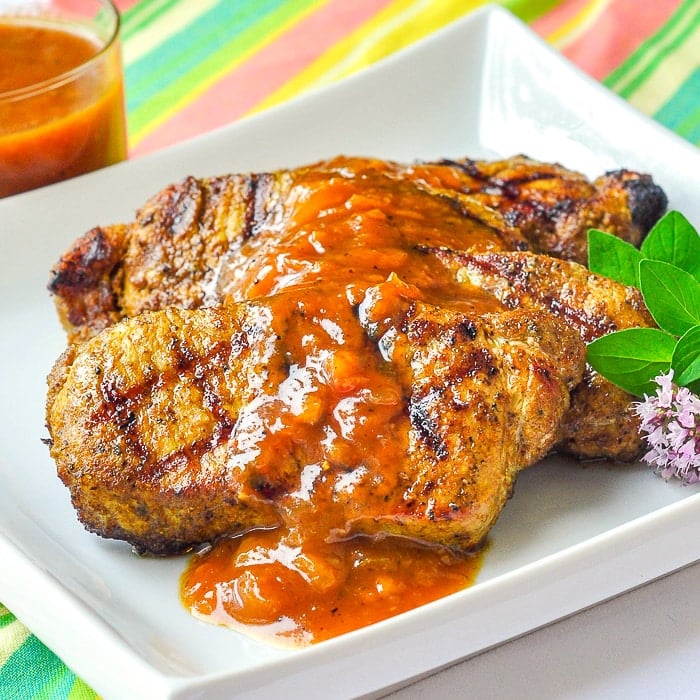 Curry Pork Chops with Easy Plum Chutney on a white plate with oregano garnish