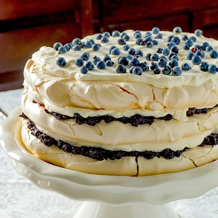 Close up photo of blueberry pavlova cake on a white cake stand