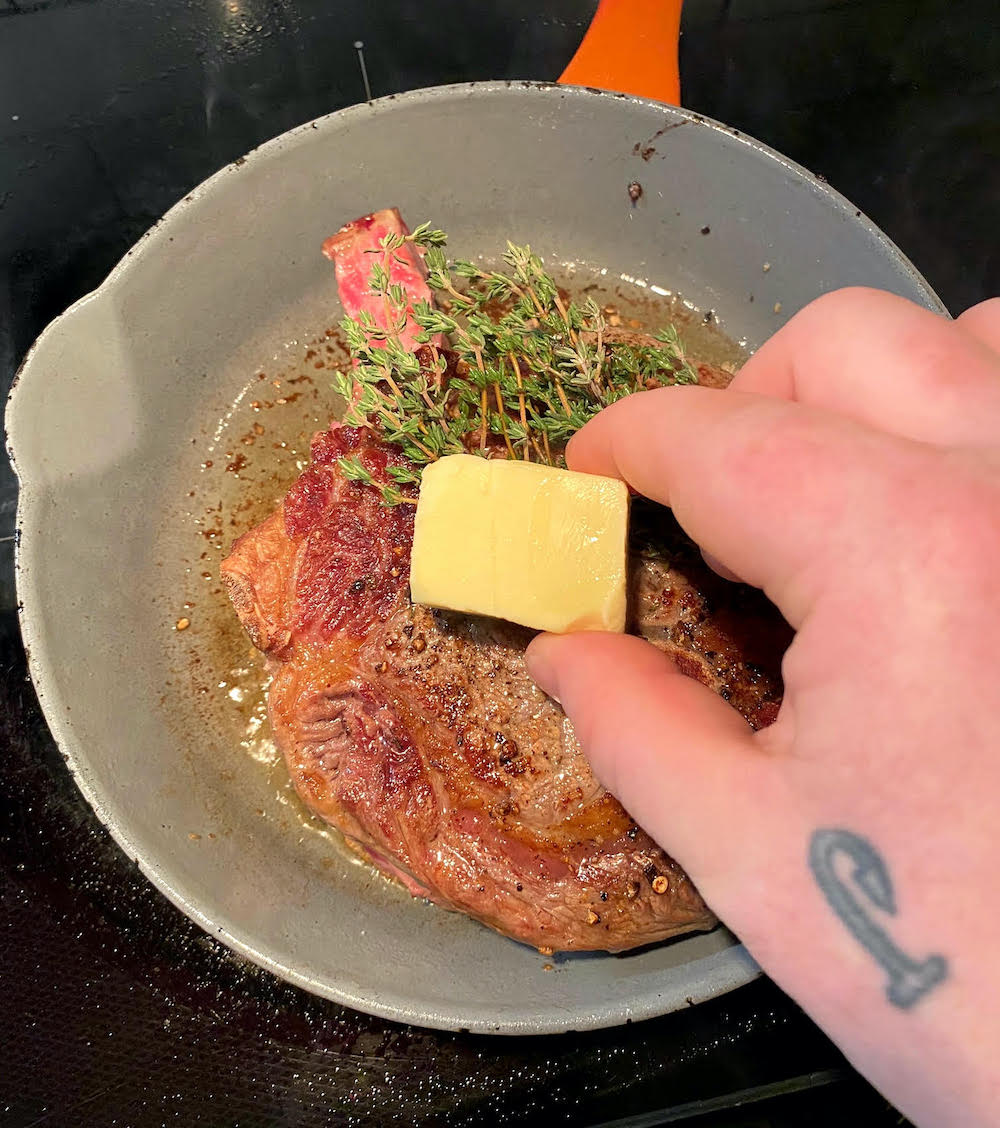 adding butter to the seared steak