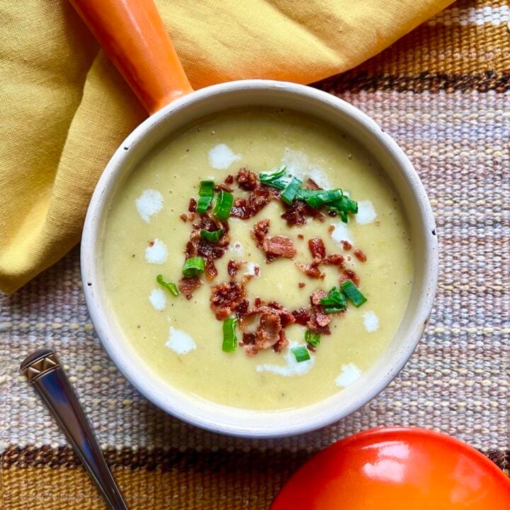 A bowl of potato leek soup in a little orange pot with a yellow napkin.