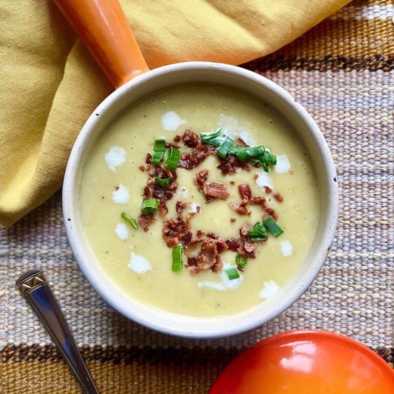 A bowl of potato leek soup in a little orange pot with a yellow napkin.