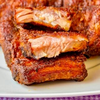 Dry Rubbed Oven Ribs stacked on a white plate.