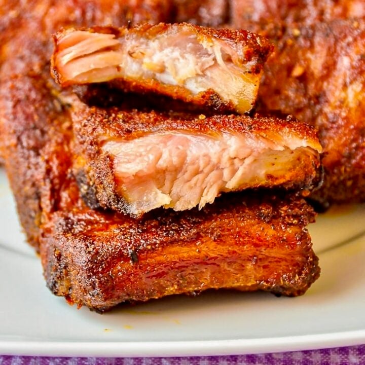 Dry Rubbed Oven Ribs stacked on a white plate.