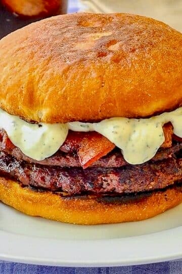 The Ultimate Newfie Touton Burger close up photo of burger on white plate with a dill pickle