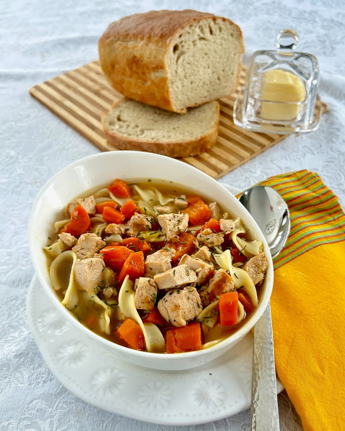 Chicken Noodle Soup overhead photo with bread and butter in background
