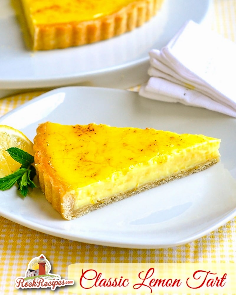 Photo of one slice of classic lemon tart on a white plate with mint and lemon garnish and title text added for social media posts.