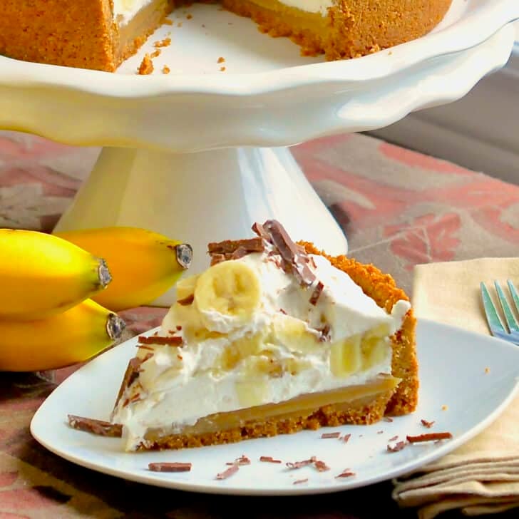 Banoffee Pie - caramel toffee, bananas, and whipped cream all in a graham cracker crumb crust!. photo of one slice with bananas in background.