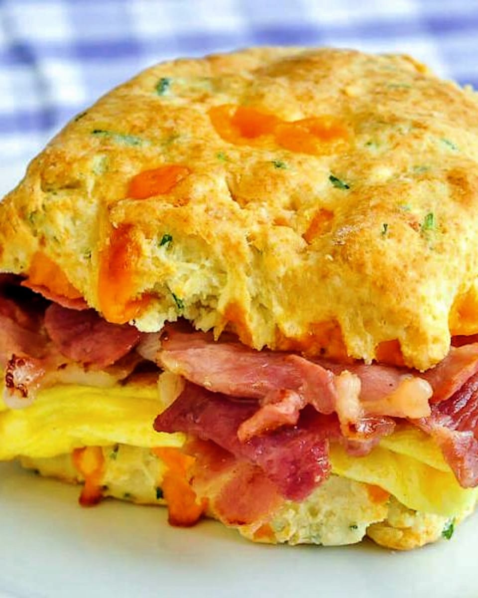 Ham Cheddar Biscuit Breakfast Sandwiches close up photo of one sandwich on a white plate on a blue checkered tablecloth