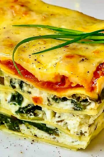 Spanakopita Lasagna close up photo of one serving on a white plate with chive garnish on top.