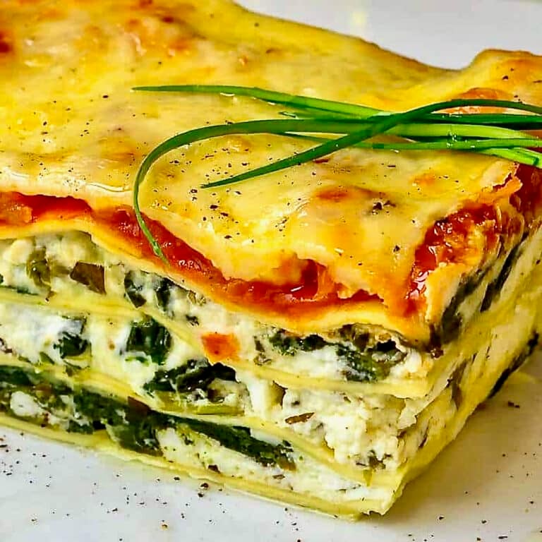Spanakopita Lasagna close up photo of one serving on a white plate with chive garnish on top.