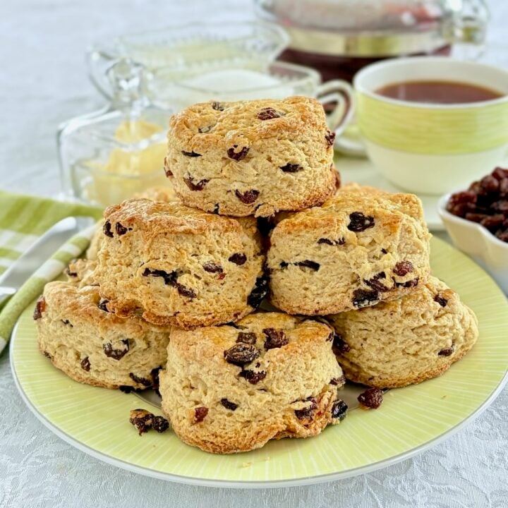Vertically cropped photo of Newfoundland Raisin Buns, stacked on a green plate with a tea service set up in the background.