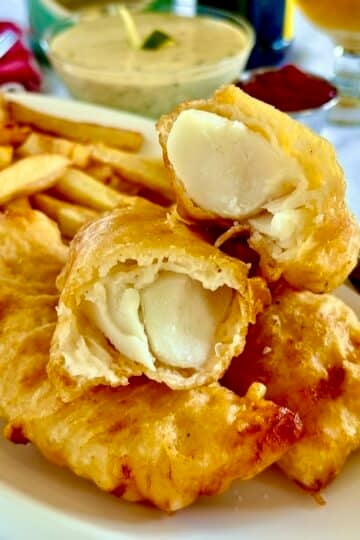 Super Crispy fish and chips close up photo of one piece of cooked fish broken open to reveal interior.