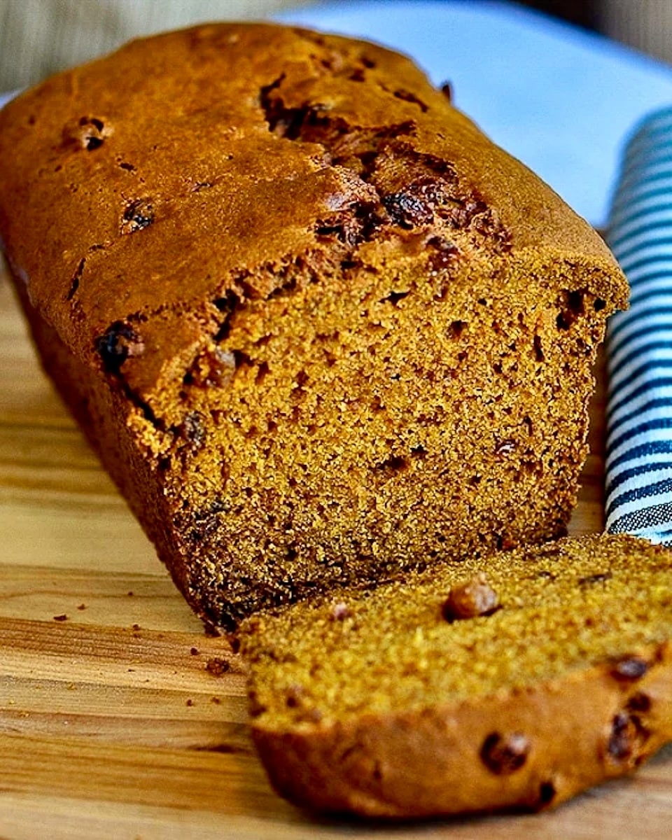 Close up photo of Pumpkin Bread with first slice cut, shown on wooden cutting board.