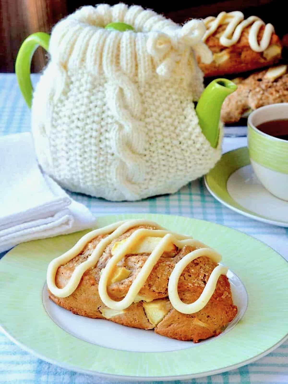 Apple Cinnamon Scones with Cream Cheese Glaze, photo of a scone on a green and white plate with coffee service in the background.