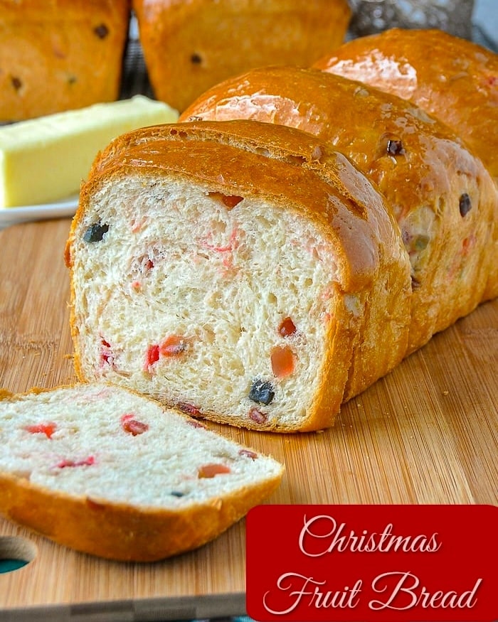 Christmas fruit bread being sliced on a wooden cutting board with title text added for social media.