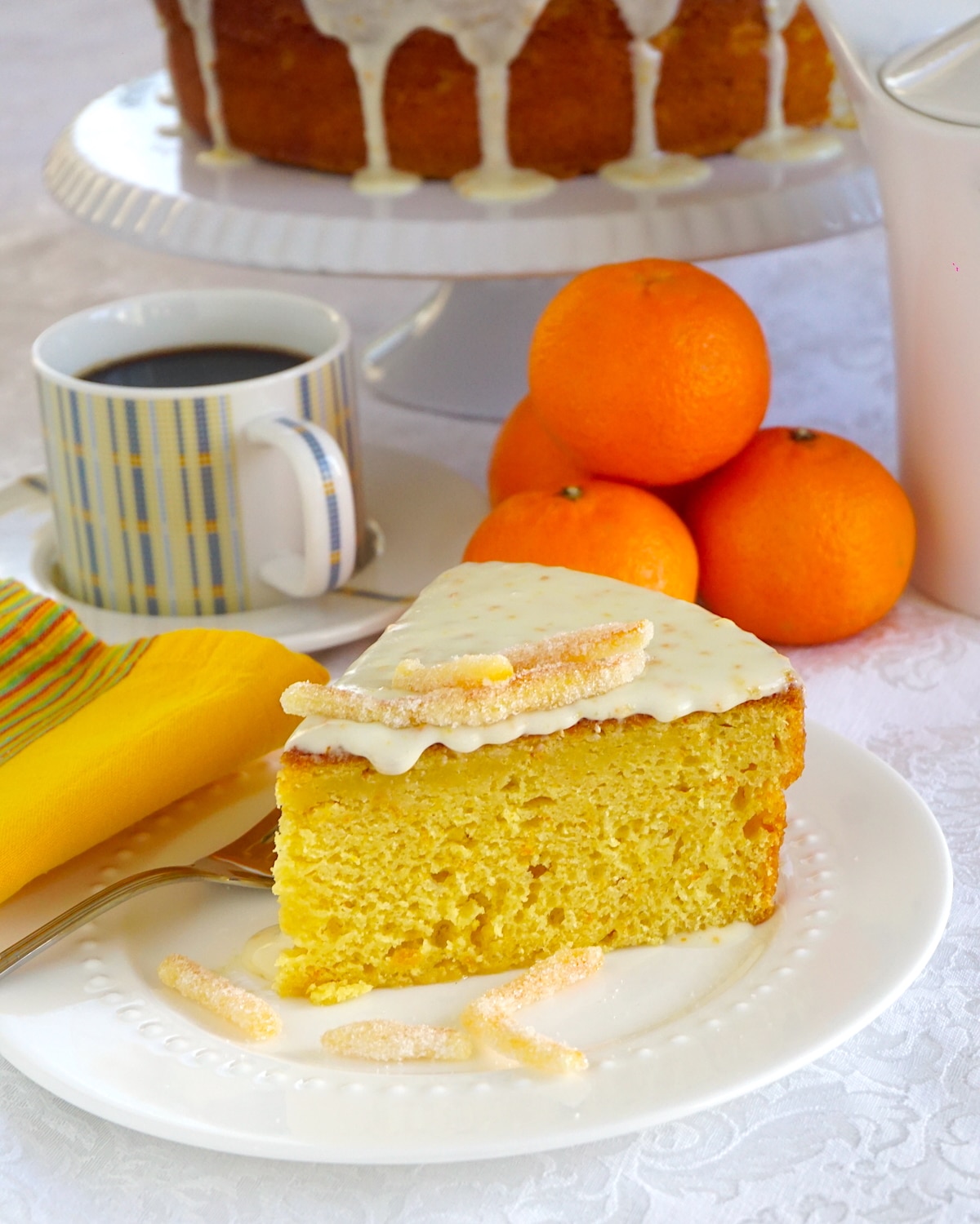 Clementine Cake photo f a slice on a white plate with clementines and whole cake in background