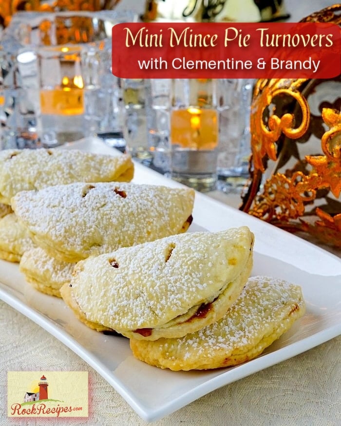 Mince Pies with clementine and brandy on a slate serving board with Christmas decorations in the background.