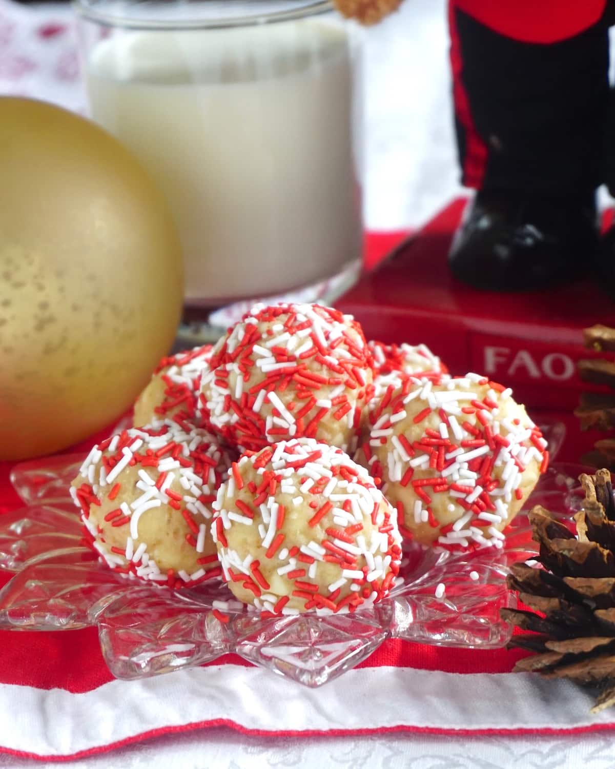 Santa Farts Cherry Almond No Bake Treat shown piled on a glass plate with a glass of milk and Christmas decorations in background