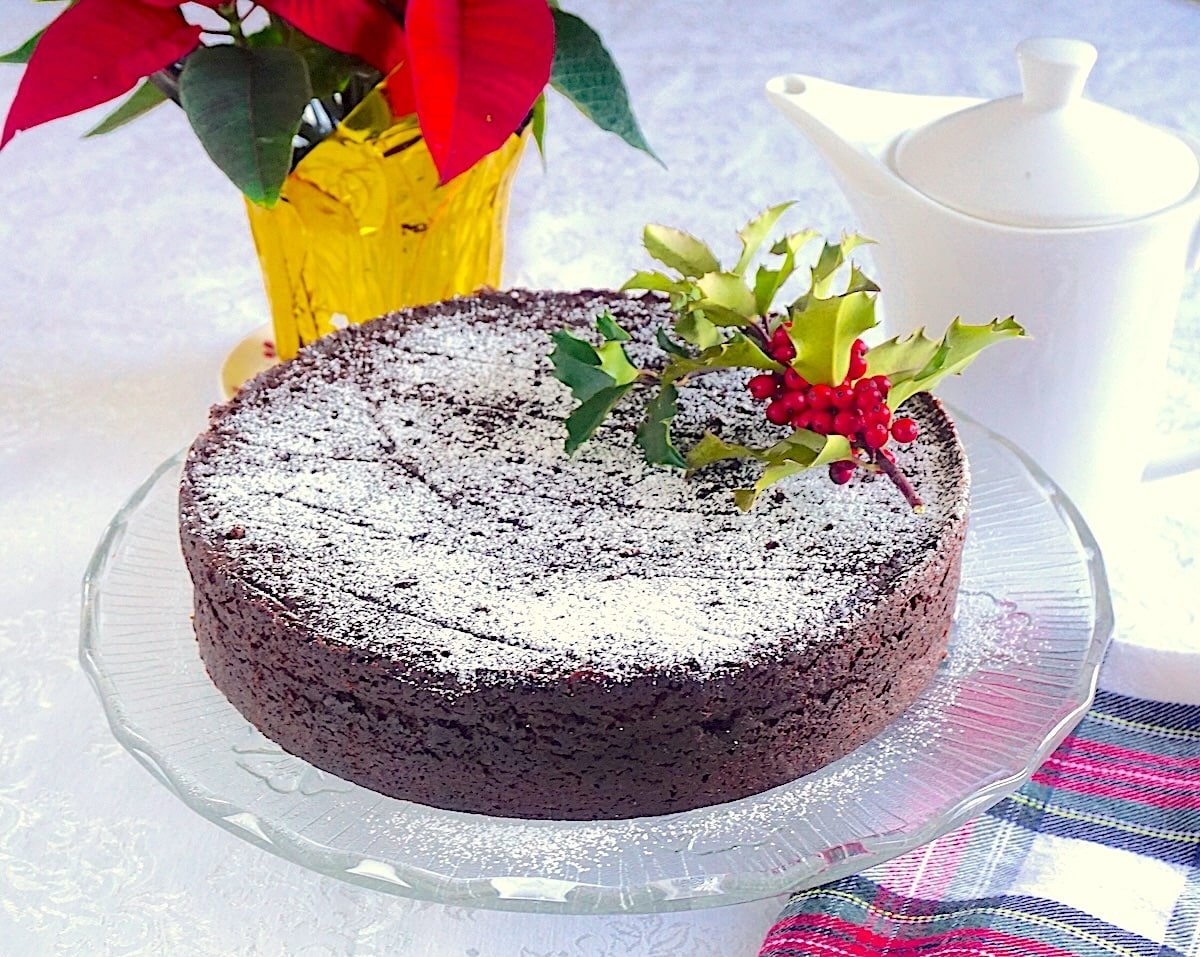 Wide shot of completed and decorated cake with Poinsettia imn background and holly sprigs on top